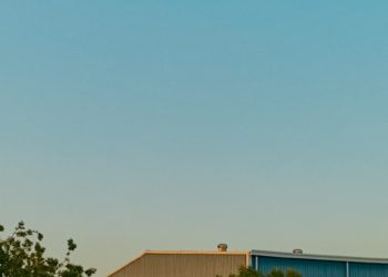 a plane flying over a building with trees in front of it