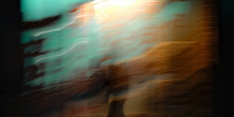 Blurred figure walking in front of a bright wall.