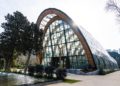 A modern glass building with a wooden arch.