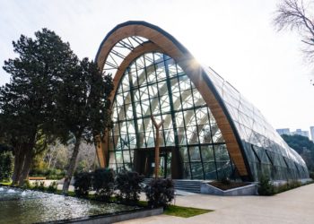 A modern glass building with a wooden arch.