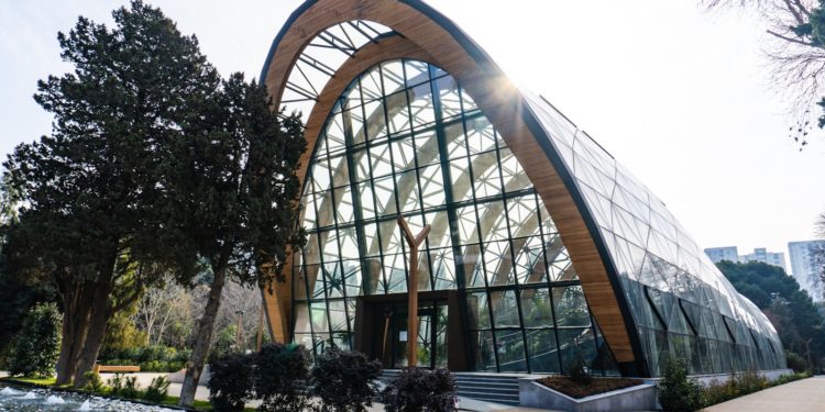 A modern glass building with a wooden arch.