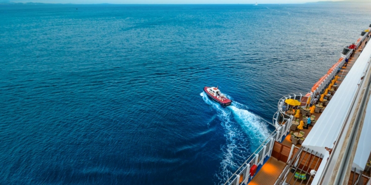 Aerial view of a luxury cruise ship with a small boat on a vast ocean at sunset.