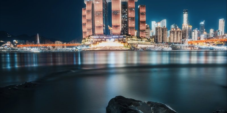 Illuminated skyscrapers reflect on the tranquil water at night.