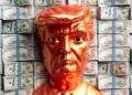 A golden trump head stands before stacks of money.