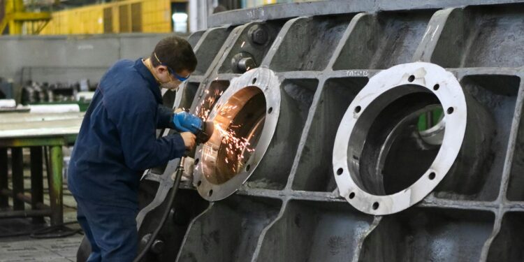 A worker in protective gear grinding metal, creating sparks in a factory setting.