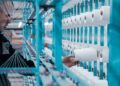 A textile factory worker inspects spools of thread on modern industrial machinery.