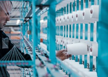 A textile factory worker inspects spools of thread on modern industrial machinery.