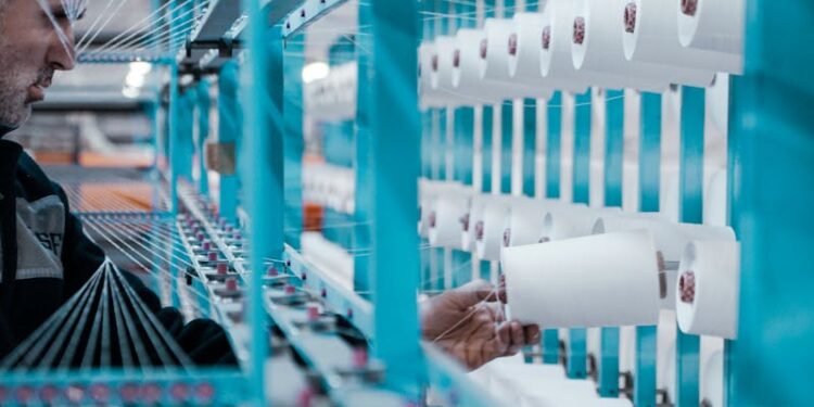 A textile factory worker inspects spools of thread on modern industrial machinery.