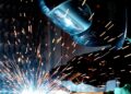 A focused welder works with metal in an industrial setting, creating vibrant sparks.