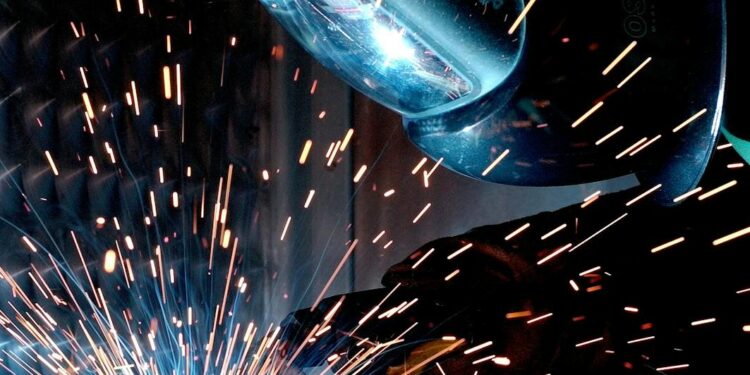 A focused welder works with metal in an industrial setting, creating vibrant sparks.