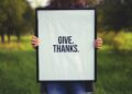 person holding rectangular black wooden photo frame with Give. Thanks. print