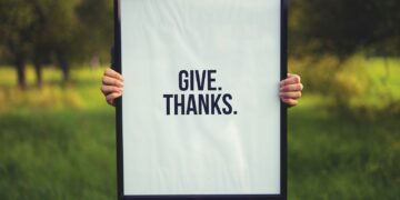 person holding rectangular black wooden photo frame with Give. Thanks. print