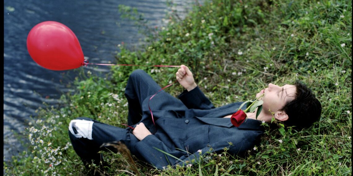 Man in suit with red balloon by water