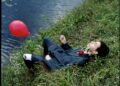 Man in suit with red balloon by water